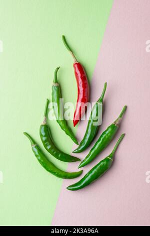 Grüne und rote Chilis auf körnigen strukturierten hellgrünen und rosa Hintergrund angeordnet, reifen und unreifen gemeinsamen Gemüse für ihren würzigen Geschmack verwendet Stockfoto