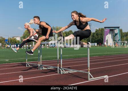 Zwei AthletInnen, Frau und Mann, die im Freien im Stadion Hürden laufen Stockfoto