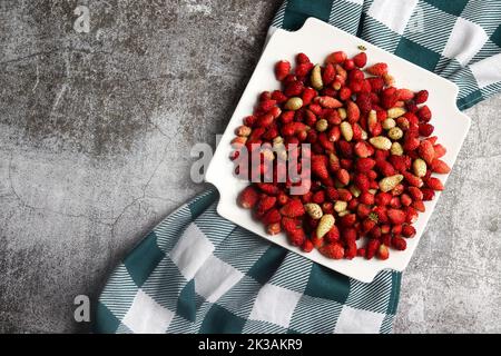 Süße wilde Erdbeeren (Fragaria vesca) auf einem weißen quadratischen Teller auf dunklem Grund. Draufsicht, flach liegend Stockfoto