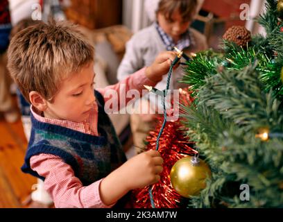 Weihnachten ist eine Zeit des kindlichen Wunders... Ein kleiner Junge, der einen Weihnachtsbaum schmückt. Stockfoto