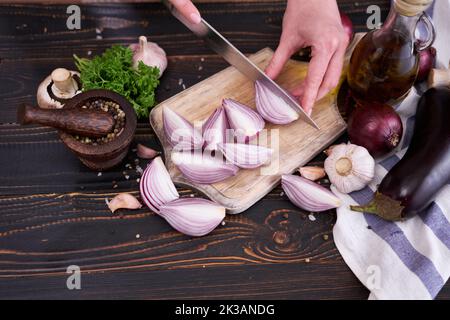 Frau schneidet rote Zwiebel auf Holz Schneidebrett mit dunklem Hintergrund Stockfoto