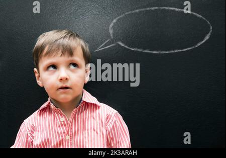 Helfen Sie Ihrem Kind, seine Stimme zu finden... Ein kleiner Junge, der vor einer Tafel mit einer Sprechblase auf der Tafel steht. Stockfoto