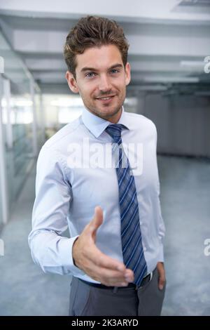 Willkommen in der Firma. Ein hübscher junger Geschäftsmann bietet Ihnen seine Hand im Büro. Stockfoto