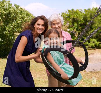 Lasst mich hoch gehen. Ein kleines Mädchen wird auf einer Schaukel nach draußen geschoben. Stockfoto