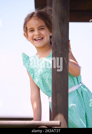 Sie spielt gerne draußen. Porträt eines kleinen Mädchens, das an einem sonnigen Tag in einem Dschungelgymnastik spielt. Stockfoto