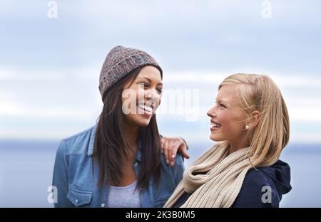 Freundschaft und Lachen können jeden Tag aufhellen. Zwei glückliche junge Frauen lächeln am Strand. Stockfoto