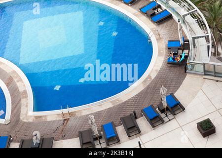 Abu Dhabi, Vereinigte Arabische Emirate - 8. April 2019: Blauer Pool aus der Luft, ein Mann entspannt sich in einer Liege Stockfoto