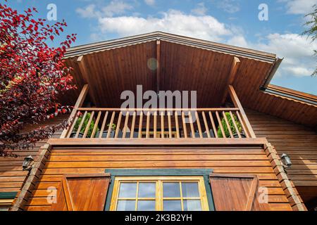 Die Fassade eines Holzhauses mit Fenster, Terrasse und Dach, gegen den blauen Himmel, Blick von unten. Stockfoto