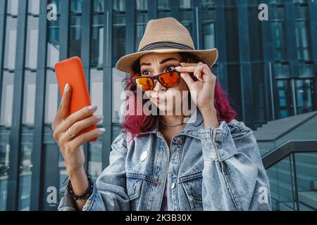 Mädchen schaut überrascht und lustig auf den Bildschirm ihres Telefons. Das Konzept der unerwarteten virtuellen Kommunikation und Schockinhalte Stockfoto