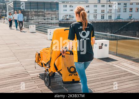 23. Juli 2022, Düsseldorf, Deutschland: Postbote mit Post-Zustellung gelber Wagen an der Stadtstraße. Beruf und internationale Briefzustellung Stockfoto