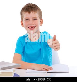 Ich studiere gerne hart. Porträt eines jungen Jungen, der mit seinen Hausaufgaben ein Daumen hoch hält. Stockfoto