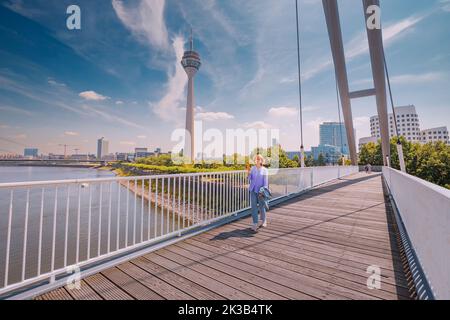 Mädchen, die über eine Fußgängerbrücke über den Rhein laufen und auf den berühmten Düsseldorfer Fernsehturm blicken. Reiseziele und Sehenswürdigkeiten Stockfoto