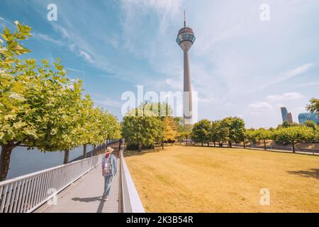 Mädchen, die über eine Fußgängerbrücke über den Rhein laufen und auf den berühmten Düsseldorfer Fernsehturm blicken. Reiseziele und Sehenswürdigkeiten Stockfoto