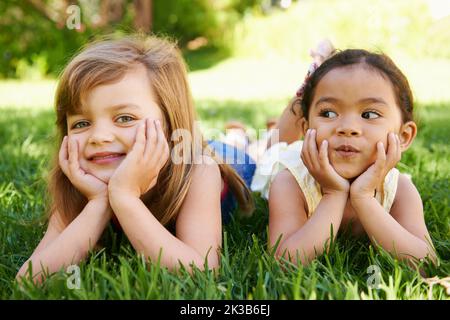 Die Sommertage verwelken zusammen. Zwei entzückende kleine Mädchen liegen nebeneinander auf dem Gras. Stockfoto