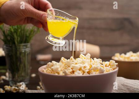 Geschmolzene Butter wird in einer Tonschüssel auf dem Küchentisch auf Popcorn gegossen Stockfoto