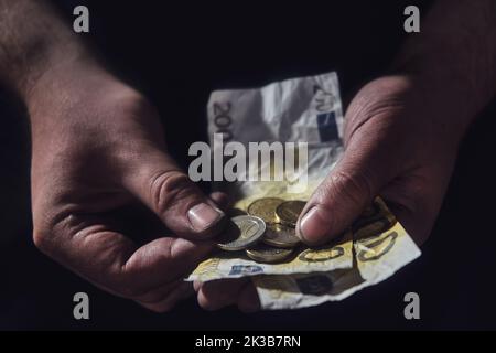 Mann hält Euro-Geld auf schwarzem Hintergrund, Nahaufnahme. Europäisches Bargeld in den schmutzigen Händen eines armen Mannes vor dunklem Hintergrund Stockfoto