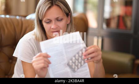 Junge Frau hält eine Packung Pillen und liest die medizinischen Anweisungen Stockfoto