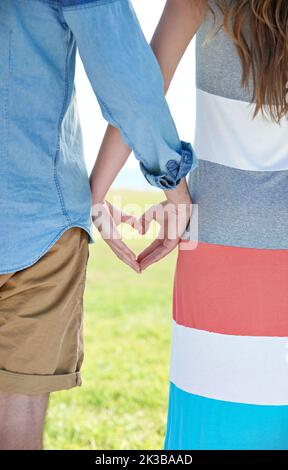 Junge Liebe. Zwei junge Menschen, die ihre Hände zusammenlegen, um eine Herzform zu bilden. Stockfoto
