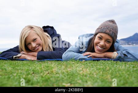 Ich verbringe einige Zeit mit meinem besten Freund. Zwei junge Frauen lächeln, während sie draußen auf dem Rasen liegen. Stockfoto