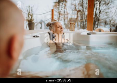 Ältere Frau genießt mit ihrem Mann an kalten Wintertagen auf der Terrasse eine Badewanne im Freien. Stockfoto