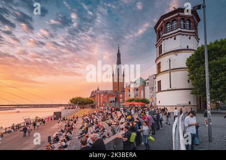 22. Juli 2022, Düsseldorf, Deutschland: Die Menschen entspannen sich und genießen den Auftritt von Straßenmusikern und den Sonnenuntergang über dem Rhein in der Nähe der Altstadt Stockfoto
