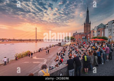 22. Juli 2022, Düsseldorf, Deutschland: Die Menschen entspannen sich und genießen den Auftritt von Straßenmusikern und den Sonnenuntergang über dem Rhein in der Nähe der Altstadt Stockfoto