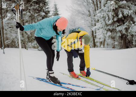 Seniorenpaar, das Ski anlegt und sich auf die Fahrt in der winterverschneiten Natur vorbereitet. Stockfoto