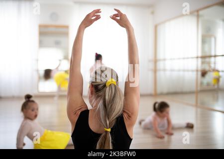 Lecteur im Balletttanz-Studio beim Stretching mit kleinen behinderten Mädchen. Konzept der Integration und Bildung behinderter Kinder. Stockfoto