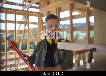 Zimmermann überprüft Holzbretter mit Wasserwaage, diy umweltfreundliche Häuser Konzept. Stockfoto