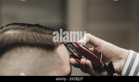 Nahaufnahme des Prozesses des Haarschneidens im Friseursalon. Qualifizierter Friseur hält Haarschneider in den Händen und korrigiert die Haarform für Männer Stockfoto
