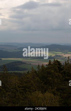 Die Sonne bildet leuchtende Flecken auf der Landschaft, die helleren Felder stehen hervor und kontrastieren mit dem dunklen Wald. Stockfoto