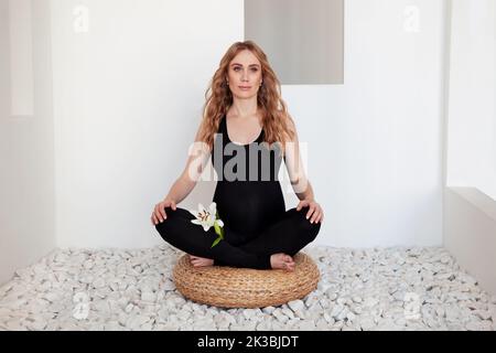 Schöne sportliche Schwangere, die in Lotusposition auf dem Boden sitzt, meditiert oder Pilates-Übungen im Spa macht. Yoga, Fitness Stockfoto