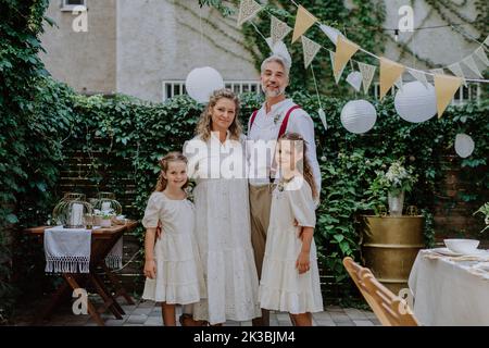 Reife Braut und Bräutigam posieren mit ihren Töchtern bei der Hochzeitsfeier draußen im Hinterhof. Stockfoto
