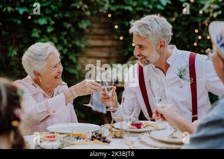 Reifer Bräutigam beim Hochzeitsempfang draußen im Hinterhof mit seiner Schwiegermutter toasten. Stockfoto