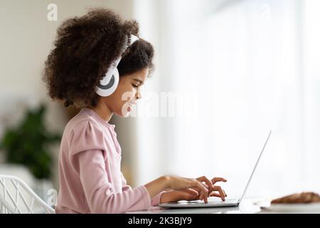 Seitenansicht eines kleinen schwarzen Mädchens, das auf der Laptop-Tastatur tippt Stockfoto