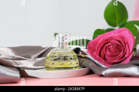 Parfümflasche, blumiger leichter Duft für Frau. Rosa Rose, Aromaspray neben Seidenbettlaken. Stockfoto