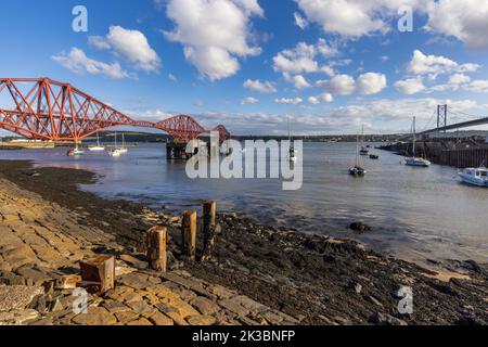 Ebbe am North Queensferry Harbour, mit den mächtigen Forth-Brücken, die sich über den Firth of Forth ausbreiten und den Norden und Süden von Queensferry verbinden. Stockfoto