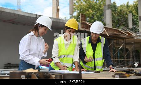 Team aus Ingenieuren, Managern und Bauarbeitern, die auf der Baustelle Plandetails besprechen Stockfoto