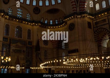 Suleymaniye Moschee mit goldfarbenem Kronleuchter, islamischem Text auf grünen Tellern in der Moschee, schönen Wanddekorationen, dunklem historischen Gebäude im Inneren Stockfoto