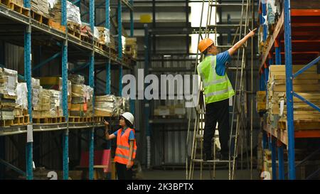 Arbeiter, die im Logistikverteilerlager mit hohen Regalen voller verpackter Kartons und Waren an der Lieferung arbeiten Stockfoto