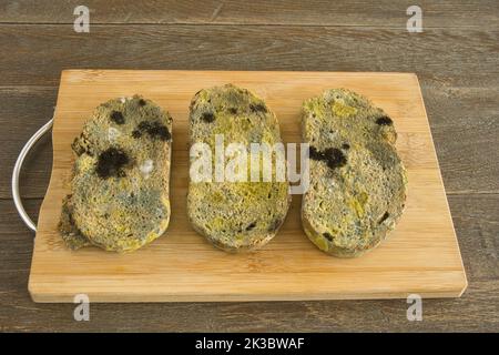 Drei Scheiben schimmeliges Brot auf Schneidebrett Stockfoto