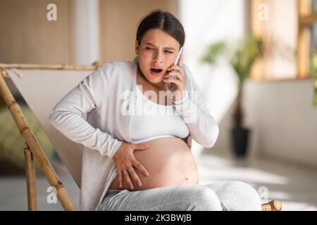 Krämpfe Während Der Schwangerschaft. Gestresste Schwangerin Berührt Bauch Und Ruft Notruf Stockfoto
