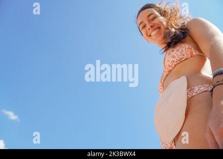 Junge Frau mit einer Ostomie-Tasche im Bikini und Blick auf die Kamera Stockfoto