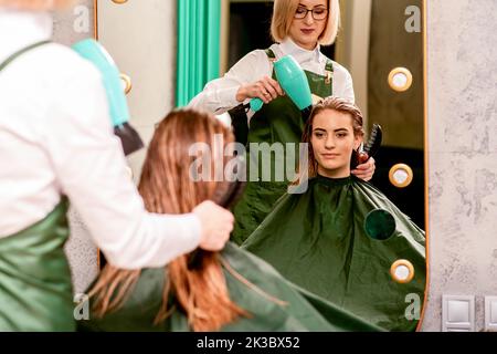 Der Friseur trocknet die Haare mit einem Haartrockner der schönen jungen kaukasischen Frau im Schönheitssalon Stockfoto