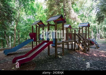 Farbenfroher Spielplatz mit Rutschen im Wald, Spielplatz für Kinder, Parks und Outdoor-Konzept, leerer Spielplatz mit Bäumen im Hintergrund Stockfoto