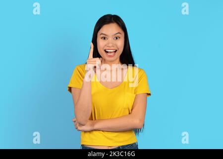 Fröhlich inspirierte junge japanische Dame in gelbem T-Shirt mit offenem Mund, zeigen Finger auf leerem Raum, bekam Idee Stockfoto