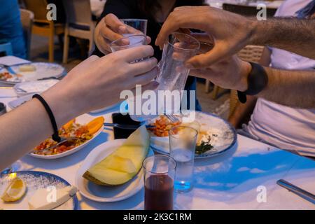 Gruppe von jungen Leuten, die türkische Raki-Gläser anklirren, traditionelle Truthahn-Vorspeisen im Hintergrund, Freunde in der türkischen Taverne, Speisen und Essensidee Stockfoto