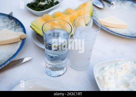 Türkisches Raki mit Wasser auf dem Tisch mit Melonenscheiben und Vorspeise, traditioneller türkischer Alkohol, bekannt als Rakı, chillen Sie mit Freunden im Restaurant Stockfoto