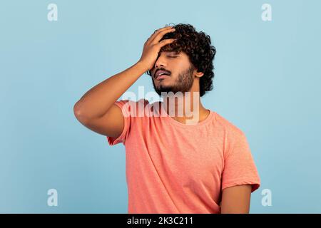 Trauriger Ostmann, der seinen Kopf berührt, blauer Hintergrund Stockfoto