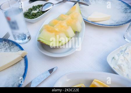 Melone auf einem Tisch mit Raki und Vorspeise, Abendessen und Mahlzeit Idee, traditionelle türkische Alkohol als Rakı bekannt, Lebensmittel auf einem Teller mit Messer Stockfoto